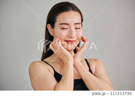 顔をマッサージして肌のお手入れをする30代女性 111313730