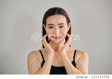 顔をマッサージして肌のお手入れをする30代女性 111313738