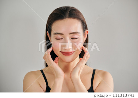 顔をマッサージして肌のお手入れをする30代女性 111313743