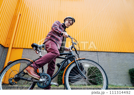 Bottom view Young stylish man in helmet riding on cruiser city Bicycle near orange Wall. Student on the way to college on bike. Eco friendly transportation for carbon footprint. Sustainable lifestyle Bottom view Young stylish man in helmet riding on cruiser city Bicycle near orange Wall. Student on the way to college on bike. Eco friendly transportation for carbon footprint. Sustainable lifestyle 111314492