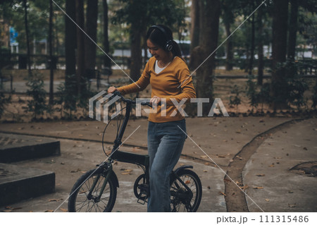 Happy young Asian woman while riding a bicycle in a city park. She smiled using the bicycle of transportation. Environmentally friendly concept. 111315486