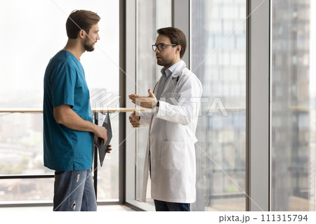 Serious doctor talking to hospital nurse man, giving instructions 111315794