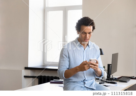 Focused handsome young Hispanic businessman typing on mobile phone Focused handsome young Hispanic businessman typing on mobile phone 111315818