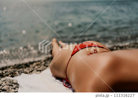 A woman sunbathes on the beach, lying on her stomach in a red swimsuit against the sea backdrop. A woman sunbathes on the beach, lying on her stomach in a red swimsuit against the sea backdrop. 111316227