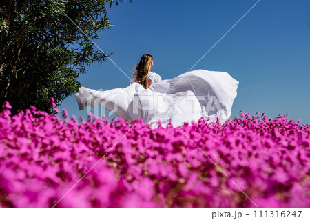 a beautiful woman in a white flowing long dress stay near a beautiful field with pink flowers rear view a beautiful woman in a white flowing long dress stay near a beautiful field with pink flowers rear view 111316247