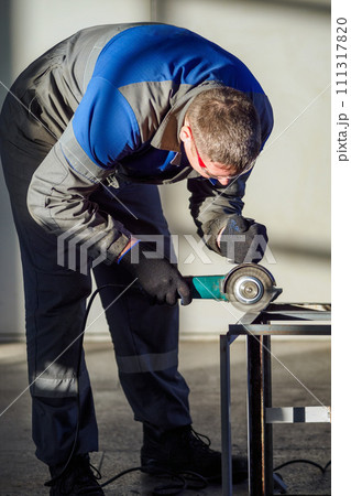 A skilled worker is shown focused on grinding a metal piece with a handheld power tool in a brightly 111317820