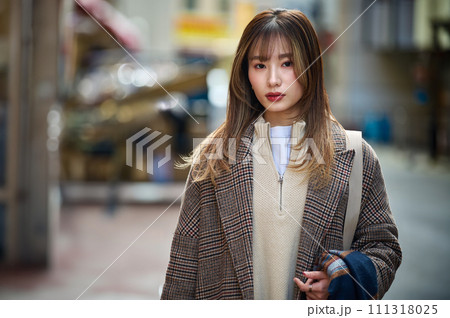 散歩するコートを着たロングヘアーの若い女性 111318025