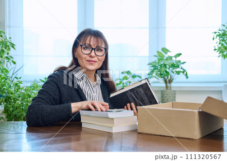 Middle-aged joyful woman with new books unpacked from cardboard box Middle-aged joyful woman with new books unpacked from cardboard box 111320567