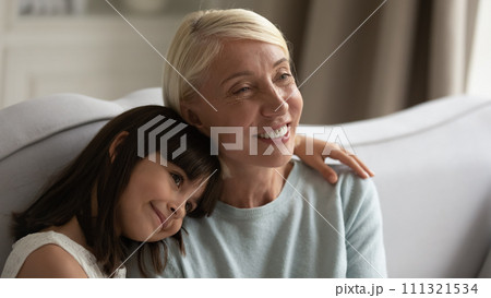 Cute little girl hugging smiling senior grandmother, sitting on couch 111321534