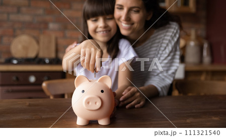 Happy hispanic mother hug preteen daughter dropping coin into piggybank 111321540