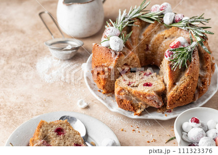 Christmas bundt cake decorated with glaze, cranberries and rosemary served on beige table. Homemade cake recipe 111323376