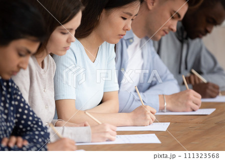 Multiracial students in row writing exam on paper Multiracial students in row writing exam on paper 111323568