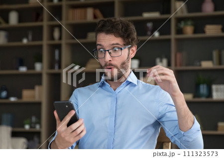 Stunned amazed guy goggle his eyes staring at smartphone screen Stunned amazed guy goggle his eyes staring at smartphone screen 111323573