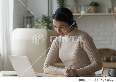 Woman listen audio course through headphones studying using laptop Woman listen audio course through headphones studying using laptop 111323653