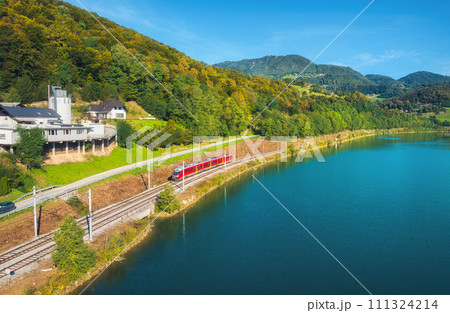 Aerial view of red train moving near river in alpine mountains Aerial view of red train moving near river in alpine mountains 111324214