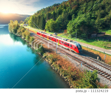 Aerial view of red train moving near river in alpine mountains Aerial view of red train moving near river in alpine mountains 111324219