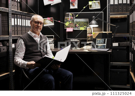 Senior investigator sitting at desk checking criminology report, working late at night at crime case in federal agency room. Fbi officer discovery mysterious suspect after analyzing victim files 111325024