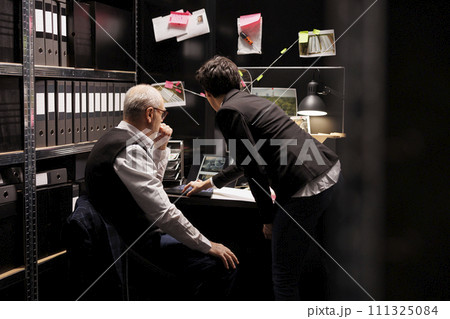 Fbi agents working at crime case analyzing investigation evidence late at night in arhive room. Private detective discussing mysterious suspect information with investigator, checking victim report 111325084