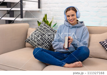 Woman listening music from headphones and reading book while sitting on sofa in living room. Woman listening music from headphones and reading book while sitting on sofa in living room. 111327168