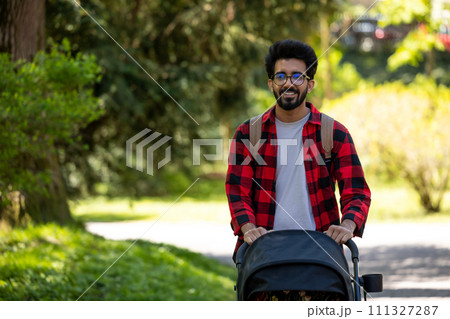 Young man in plaid shirt carrying baby carriage in the park 111327287