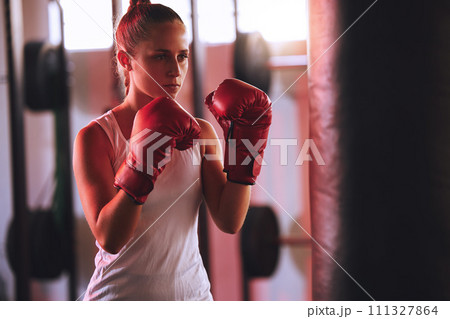 Boxer training her fitness in the gym using a punching bag practicing for a fight competition. Active, wellness and fit combat sports athlete doing a boxing workout in a health club 111327864
