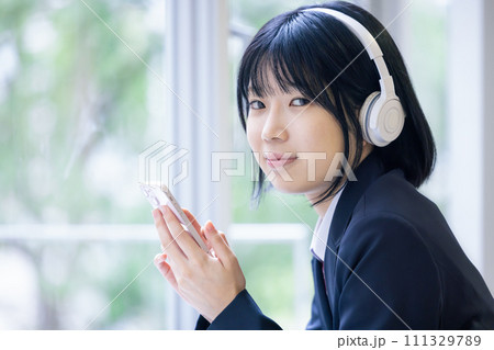 ヘッドフォンをつけてスマホを見ている女子高生　　撮影協力：有明教育芸術短期大学 111329789