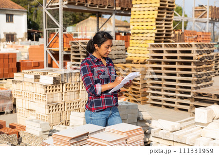 Woman manager keeps records of building materials in the open area of construction store 111331959