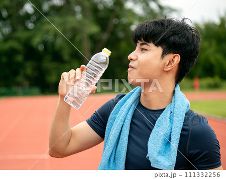 Asian Male Athlete Taking a Refreshing Water Break on Track Field; Active and Hydrated in action 111332256