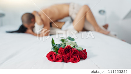 Couple, red roses and lying on bed for love, anniversary or valentines day in romance, embrace or trust at home. Romantic man and woman in bedroom intimacy, passion or bonding with flowers at house 111333223