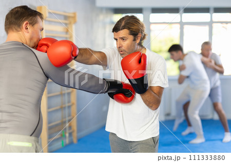 Men in boxing gloves punch deliver blow each other during training sparring session. 111333880