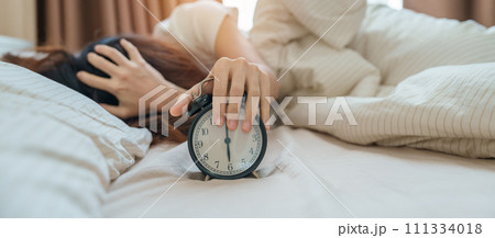 alarm clock and asian woman hand stop time in bed while sleeping, young adult female wake up late in the early morning. Relaxing , sleepy, daily routine and have a nice day concepts alarm clock and asian woman hand stop time in bed while sleeping, young adult female wake up late in the early morning. Relaxing , sleepy, daily routine and have a nice day concepts 111334018
