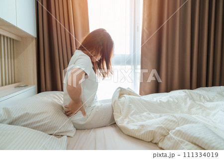 woman having back body ache during sitting on bed at home. adult female with muscle pain after Waking up due to Piriformis Syndrome, Low Back Pain and Spinal Compression. Health medical concept woman having back body ache during sitting on bed at home. adult female with muscle pain after Waking up due to Piriformis Syndrome, Low Back Pain and Spinal Compression. Health medical concept 111334019