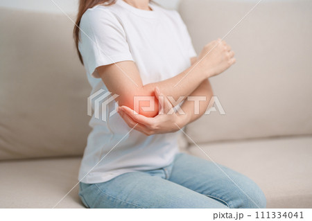 Woman having elbow ache during sitting on couch at home, muscle pain due to lateral epicondylitis or tennis elbow. injury, Health and medical concept 111334041
