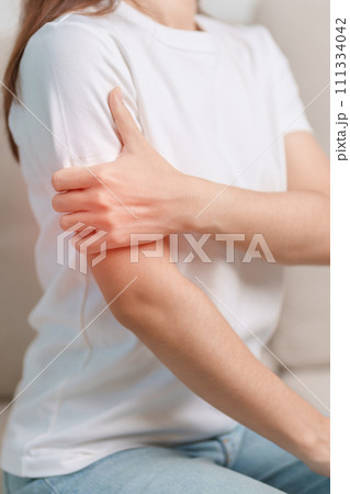 Woman having arm pain during sitting on couch at home, muscle injury and ache. Health and medical concept Woman having arm pain during sitting on couch at home, muscle injury and ache. Health and medical concept 111334042