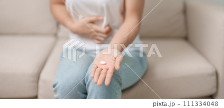 woman hand holding medicine painkiller pill and water glass on the sofa at home, taking for headaches,  stomach ache, Diarrhea Pain from food poisoning, Endometriosis, Hysterectomy and Menstrual 111334048