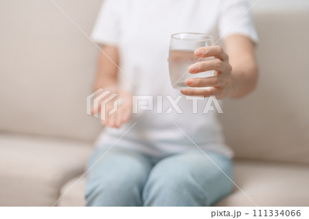 woman hand holding medicine painkiller pill and water glass on the sofa at home, taking for headaches,  stomach ache, Diarrhea Pain from food poisoning, Endometriosis, Hysterectomy and Menstrual 111334066