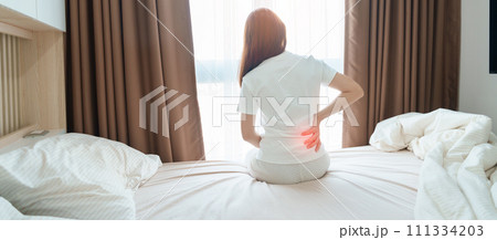 woman having back body ache during sitting on bed at home. adult female with muscle pain after Waking up due to Piriformis Syndrome, Low Back Pain and Spinal Compression. Health medical concept 111334203
