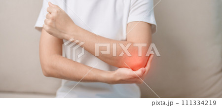 Woman having elbow ache during sitting on couch at home, muscle pain due to lateral epicondylitis or tennis elbow. injury, Health and medical concept Woman having elbow ache during sitting on couch at home, muscle pain due to lateral epicondylitis or tennis elbow. injury, Health and medical concept 111334219