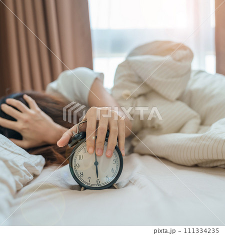 alarm clock and asian woman hand stop time in bed while sleeping, young adult female wake up late in the early morning. Relaxing , sleepy, daily routine and have a nice day concepts 111334235