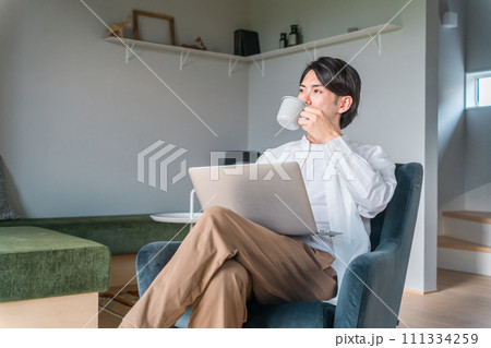 家で朝コーヒーを飲みながらノートパソコンを使う若い日本人男性(ルーティーン) 111334259