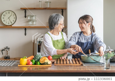 家のキッチンで一緒に料理・家事・自炊をする笑顔のアジア人高齢者女性と若い女性(家政婦・家事代行) 家のキッチンで一緒に料理・家事・自炊をする笑顔のアジア人高齢者女性と若い女性(家政婦・家事代行) 111336001