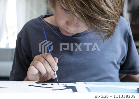 A boy, with long dark hair, draws a picture by numbers. A boy, with long dark hair, draws a picture by numbers. 111339238