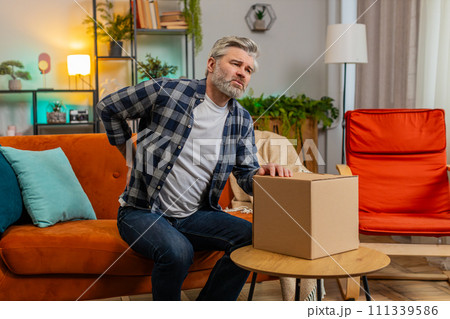 Senior mature man carrying heavy box and experiences severe back pain muscle pain of overwork spasm Senior mature man carrying heavy box and experiences severe back pain muscle pain of overwork spasm 111339586
