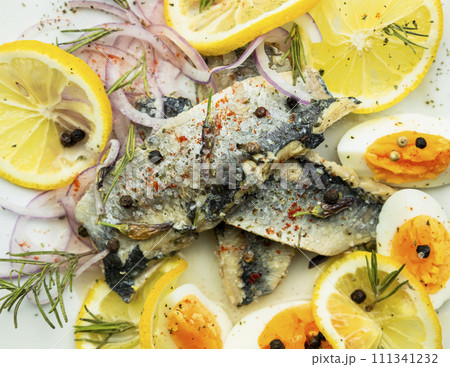 Herring fish fillets with eggs, herbs, onion and lemon on a white plate. Top view, flat lay photo 111341232