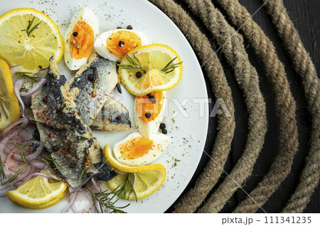 Herring fish fillets with eggs, herbs, onion and lemon on a white plate. Top view, flat lay photo 111341235