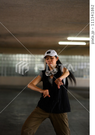Young woman hip hop dancer dancing with passion and energy in a dark parking garage 111341862