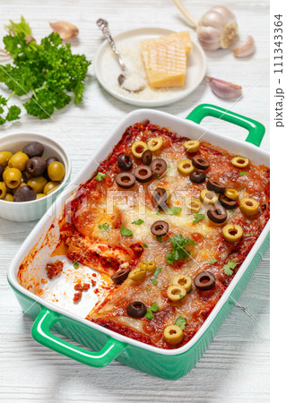 lasagna with olive rings in green baking dish 111343364