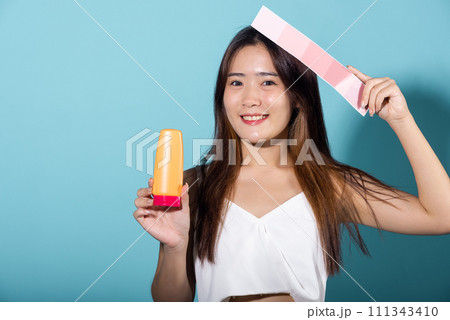 Portrait of happy female hold color card under sun protection and sun cream, Asian beautiful young woman smiling and holding skin color scale paper with suntan lotion isolated on blue background 111343410