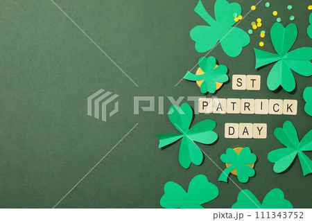 Paper clover leaves, golden coins and letters on green background, space for text 111343752
