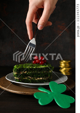 Clover leaves, coins, cake on plate and fork in hand on wooden background 111343773